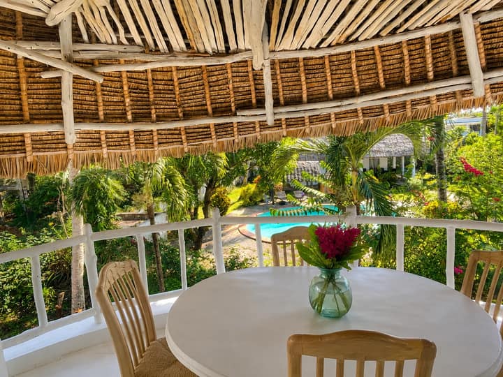 Thatched balcony at Cali Blossom Villa with a round dining table and flowers, looking over the tropical garden and pool